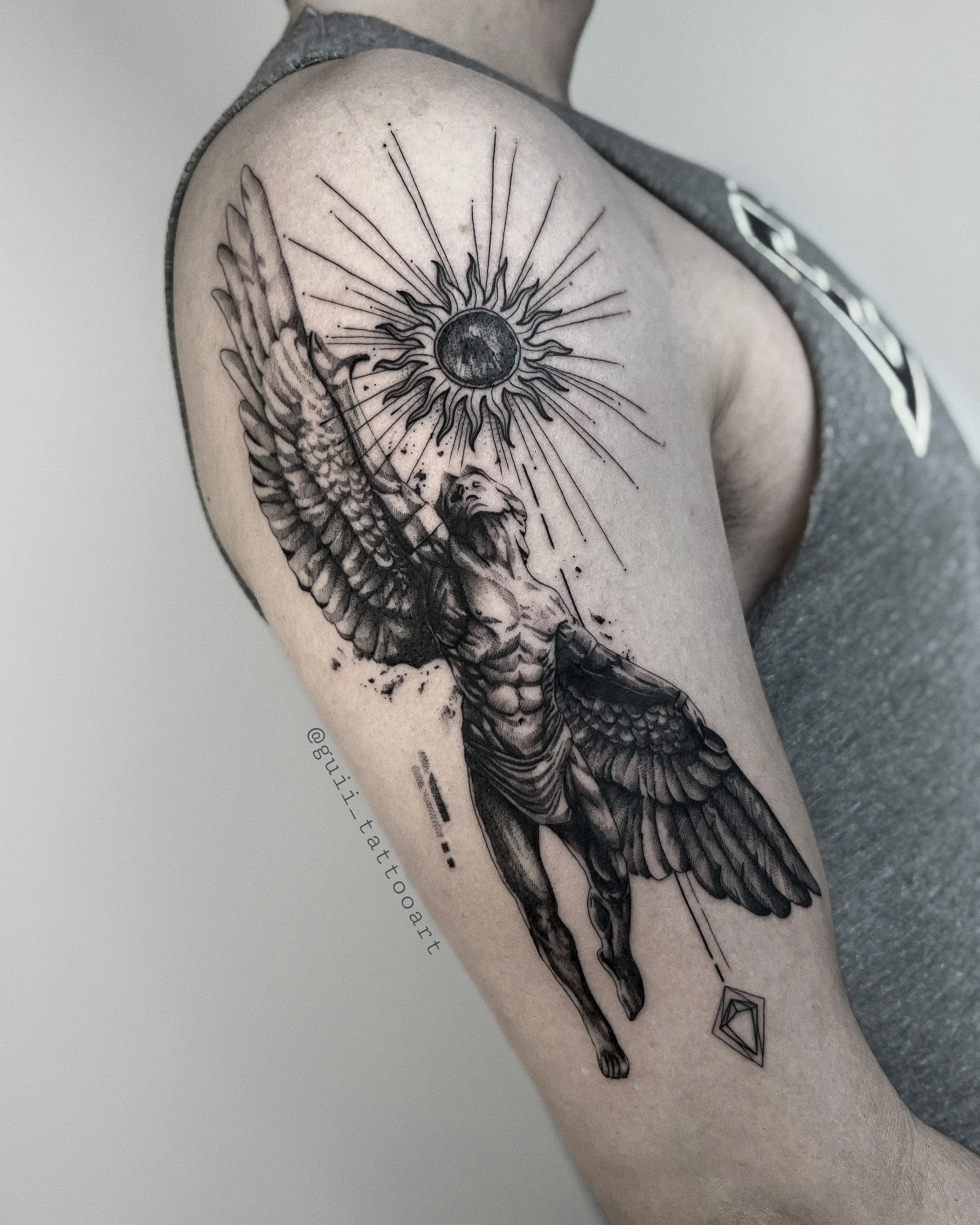 Tattoo of winged figure reaching toward stylized sun on upper arm.