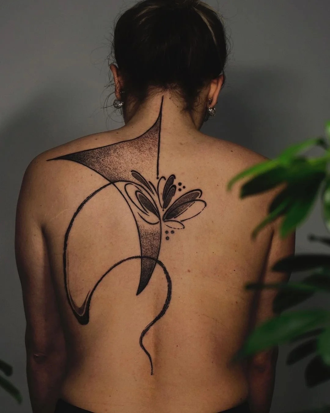 Woman with an abstract black ink tattoo on her back, featuring curved lines and dot patterns.