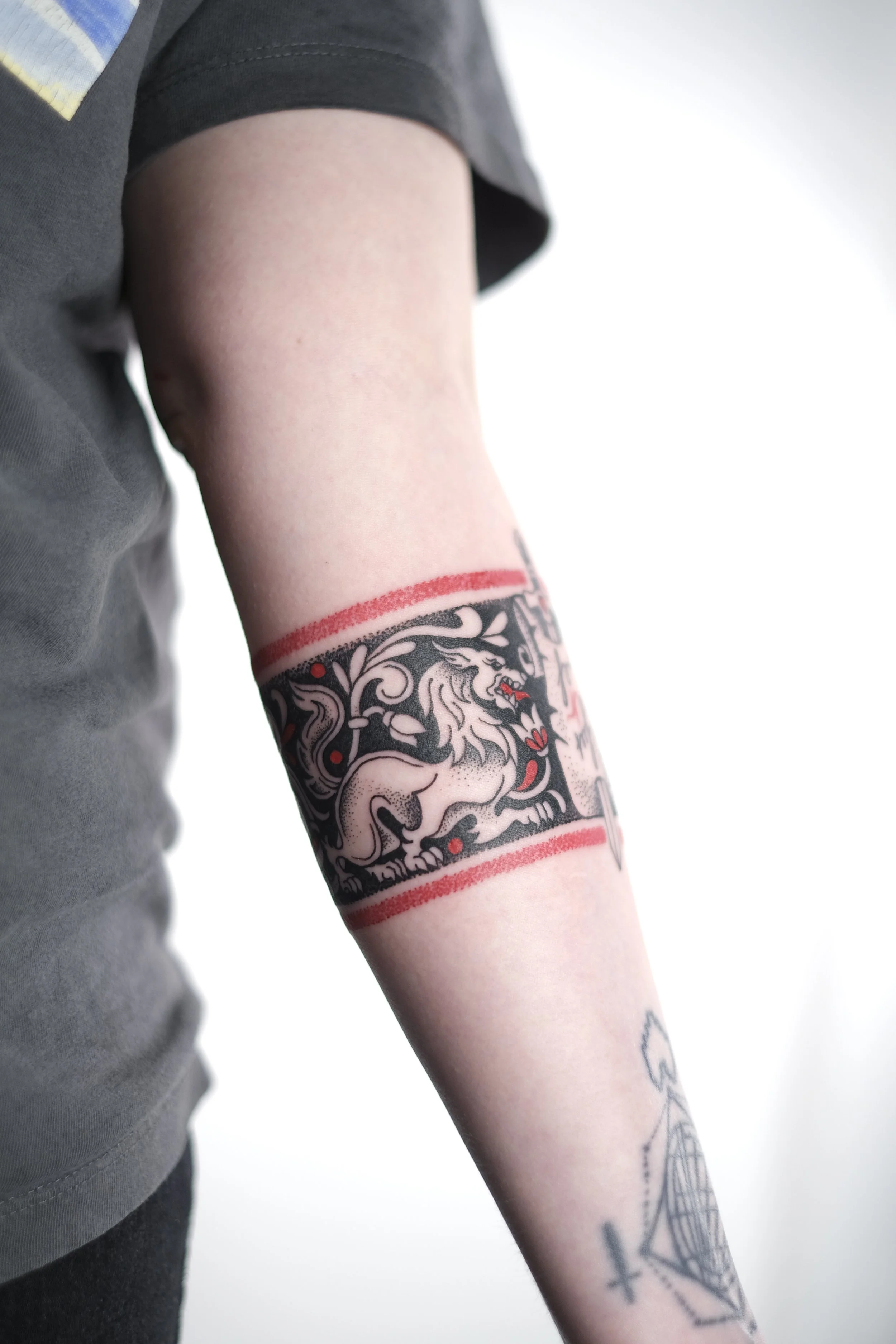 Person with a tattoo of a lion in black and white with red accents around their upper arm.