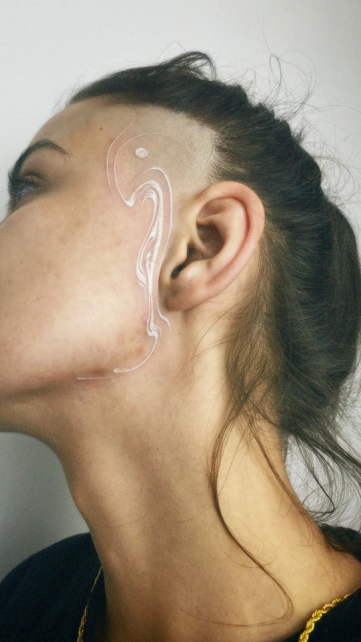 Side view of a person's face with white artistic lines painted on the temple and cheek.