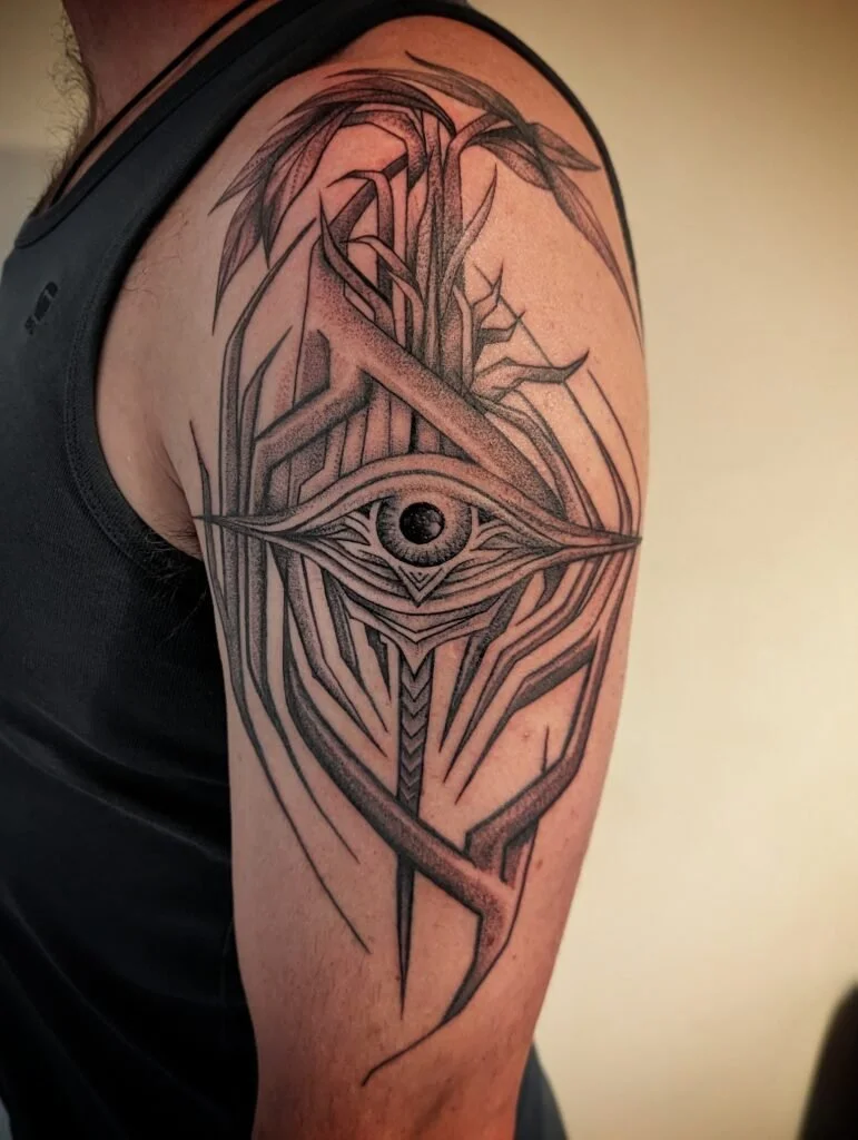 Black and gray tattoo featuring an eye with intricate geometric lines and abstract design on upper arm.