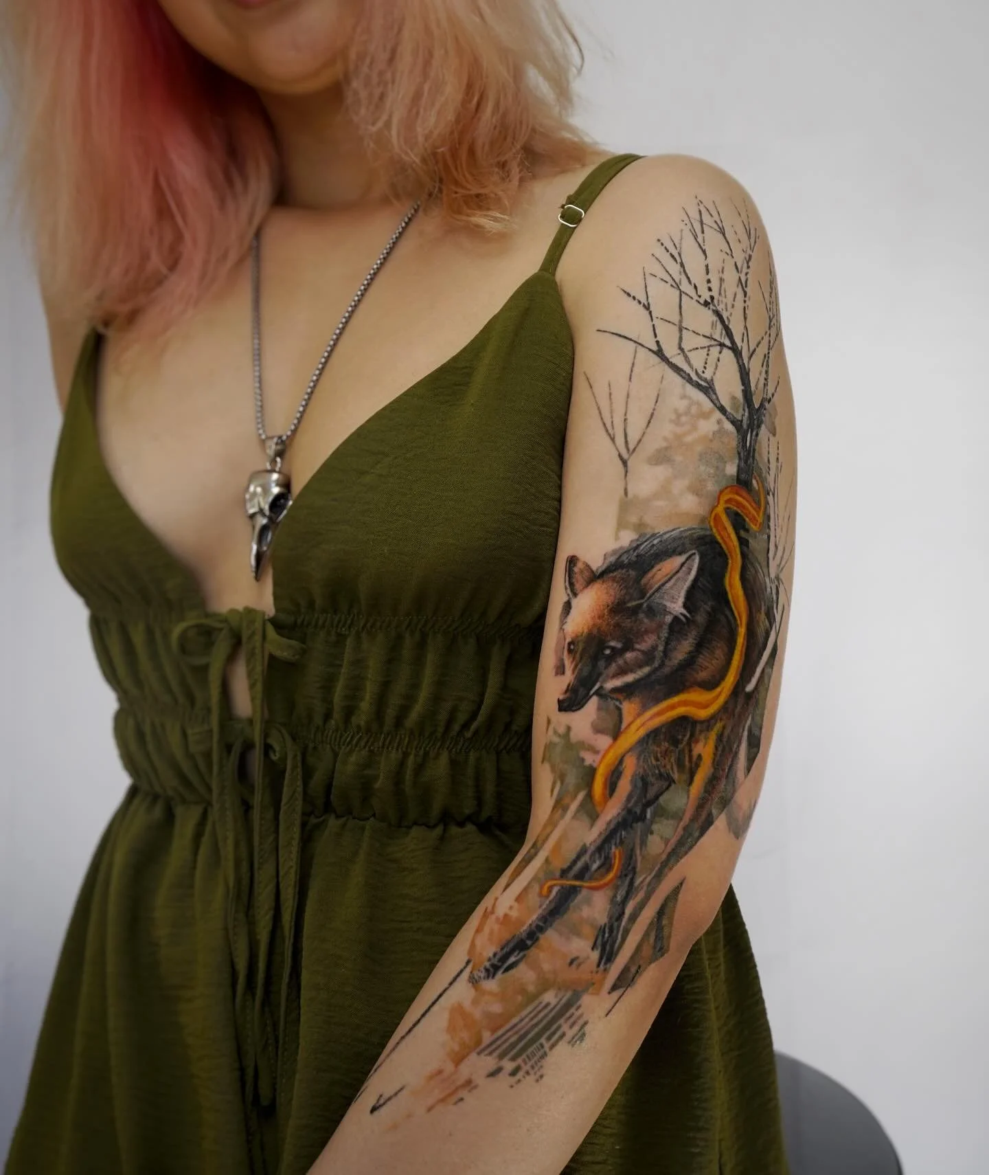Tattoo of a snarling wolf with orange accents and trees in the background on a woman's upper arm.