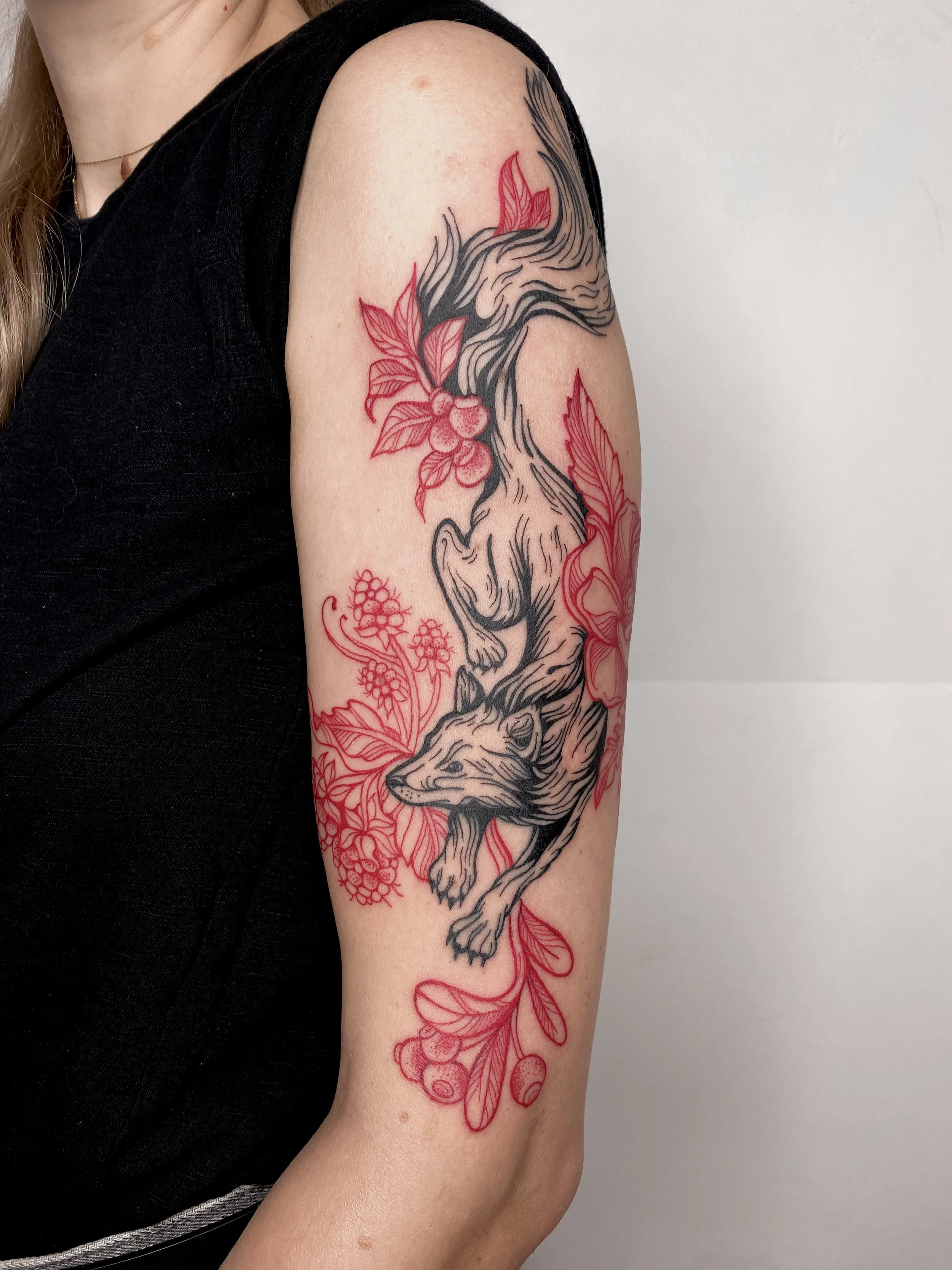 Tattoo of a fox surrounded by leaves and berries on a person's upper arm.