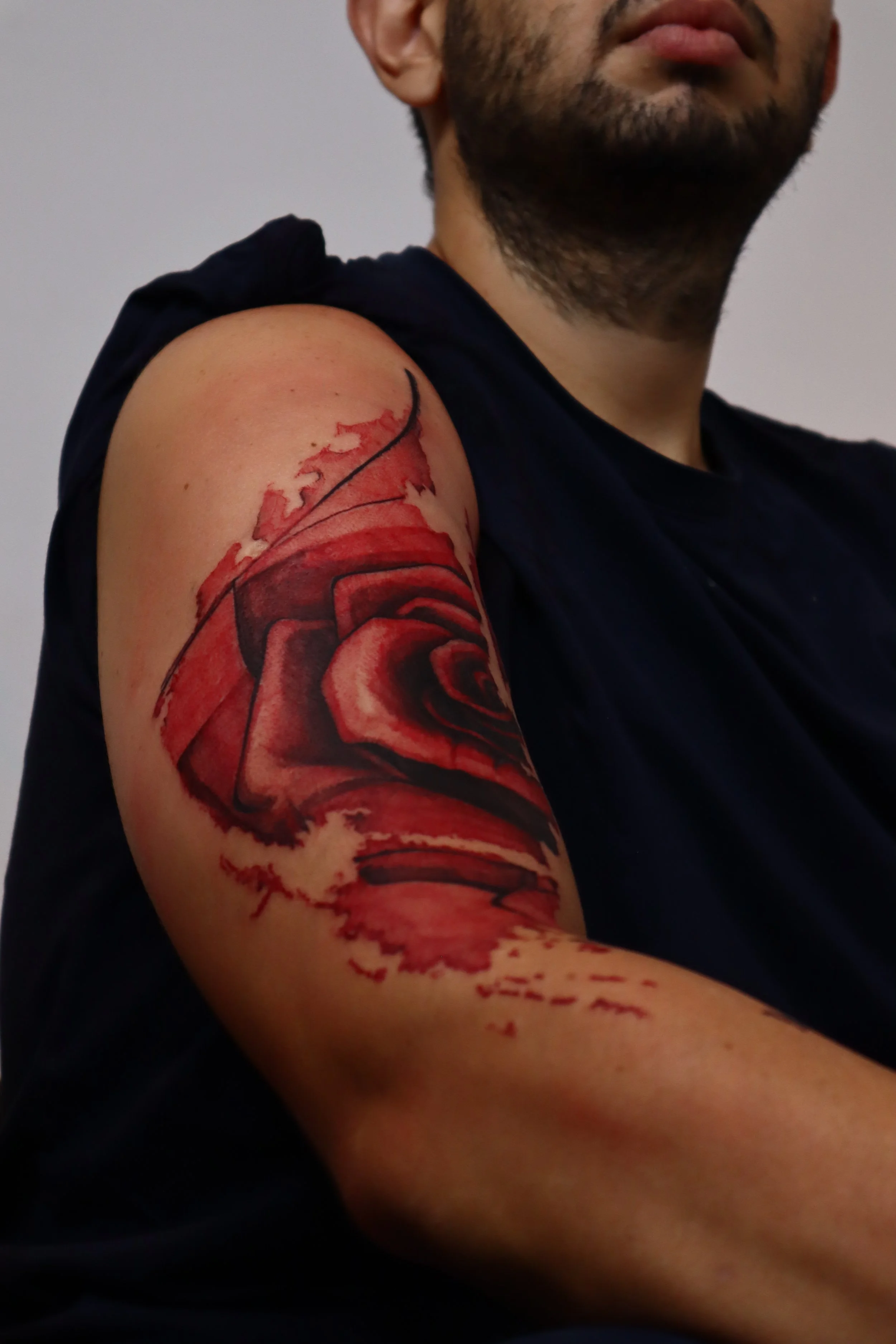 Close-up of a person's upper arm with a large, realistic red rose tattoo.