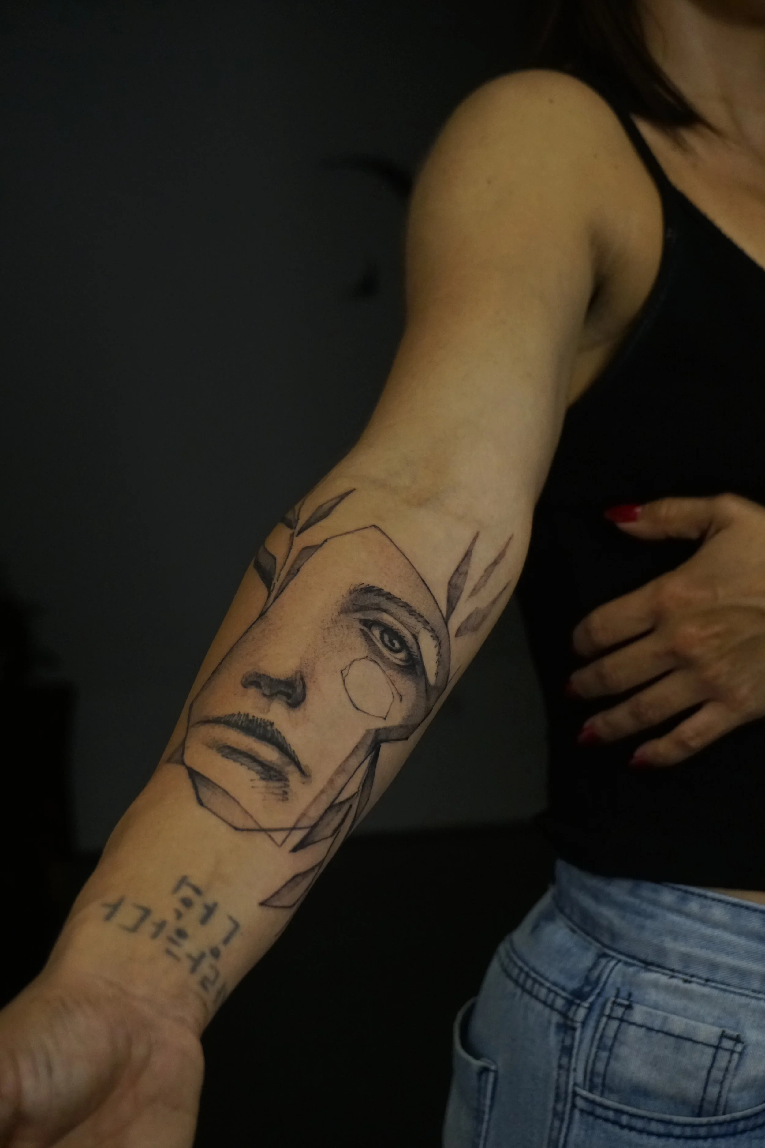 Forearm with artistic black ink tattoo of a geometric face.