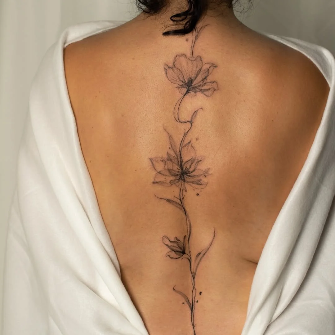 A woman's back with a vertical floral tattoo of three outlined flowers connected by a plant stem.