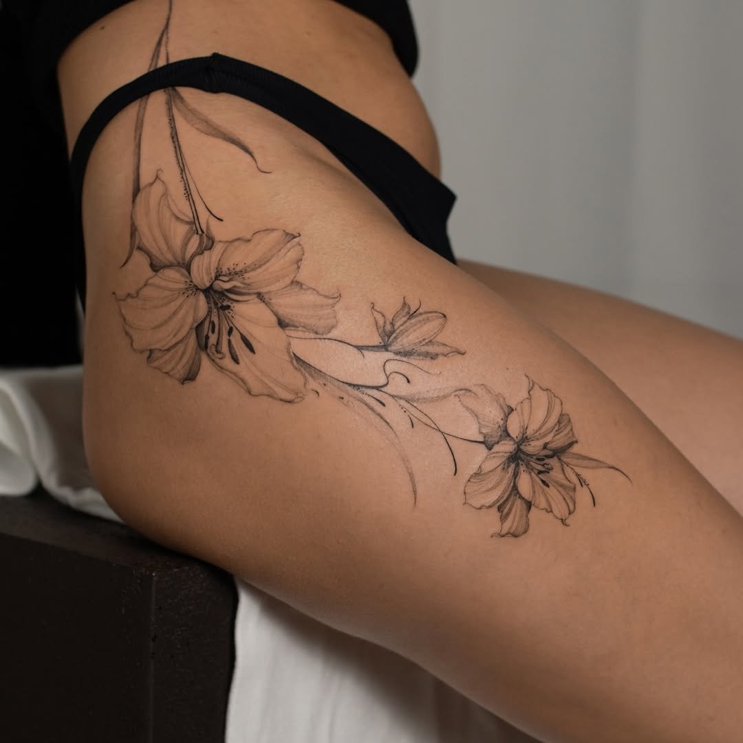 A tattoo of two large, detailed lily flowers on a person's thigh.