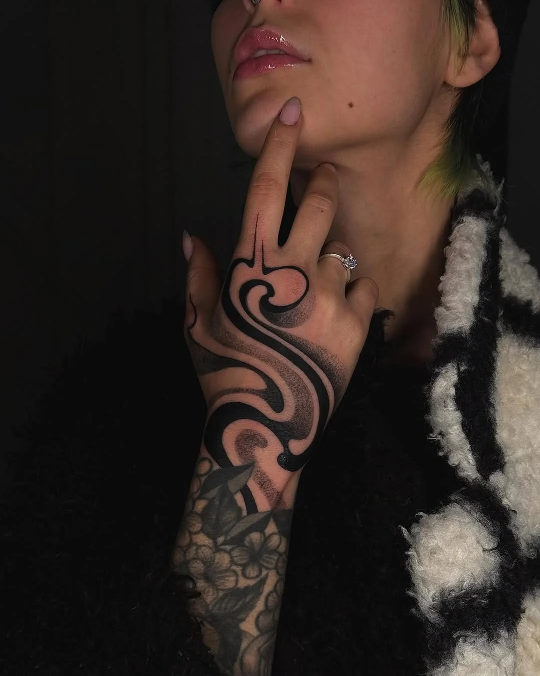Person with a black and white patterned sleeve holding their chin, displaying a bold, abstract tattoo on their hand.