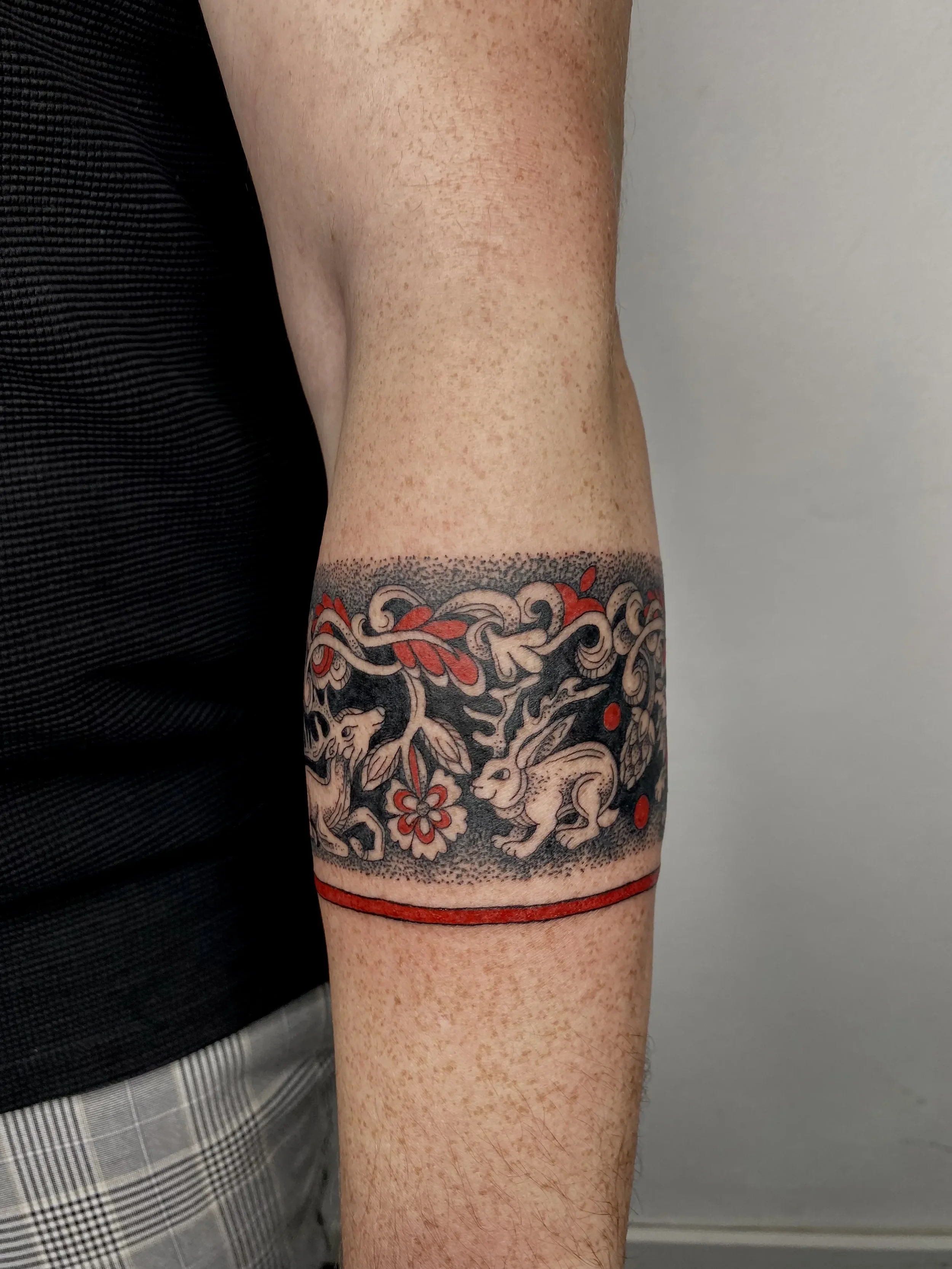 Tattoo featuring rabbits, cherry blossoms, leaves, and red accents on a person's forearm.