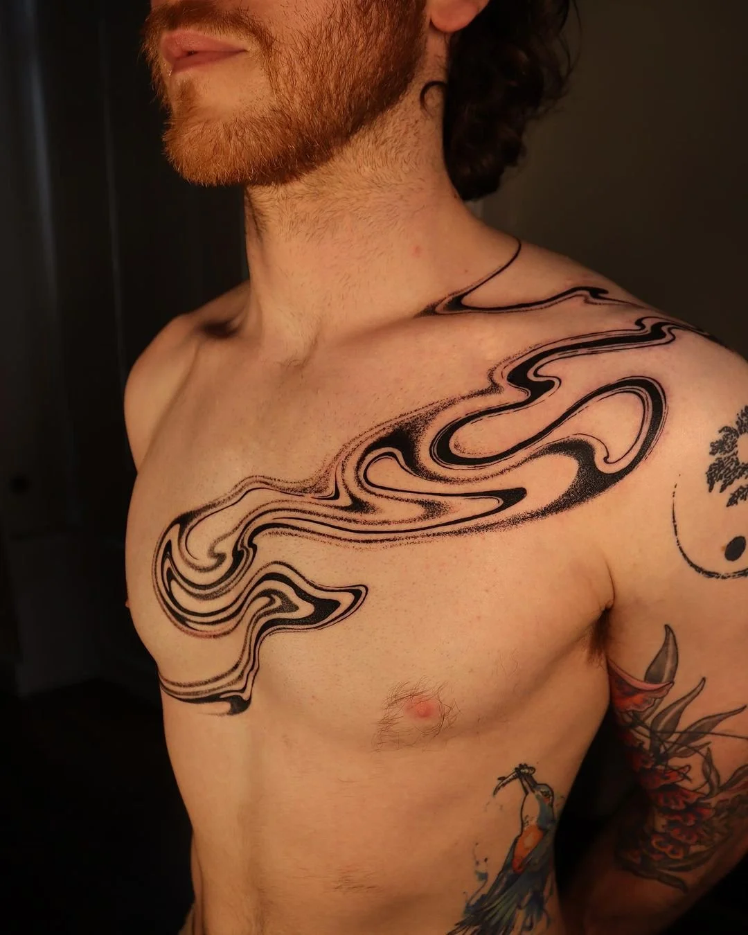 Man with abstract black swirl tattoo across chest and upper arm