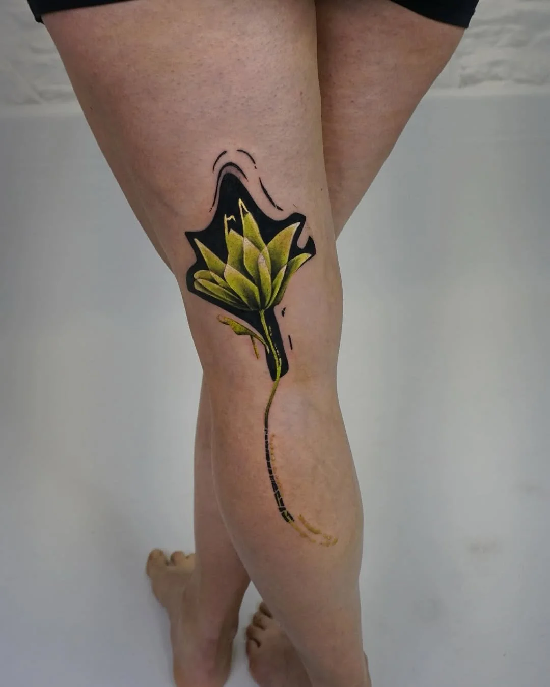 Tattoo of a yellow and black flower on a person's thigh.