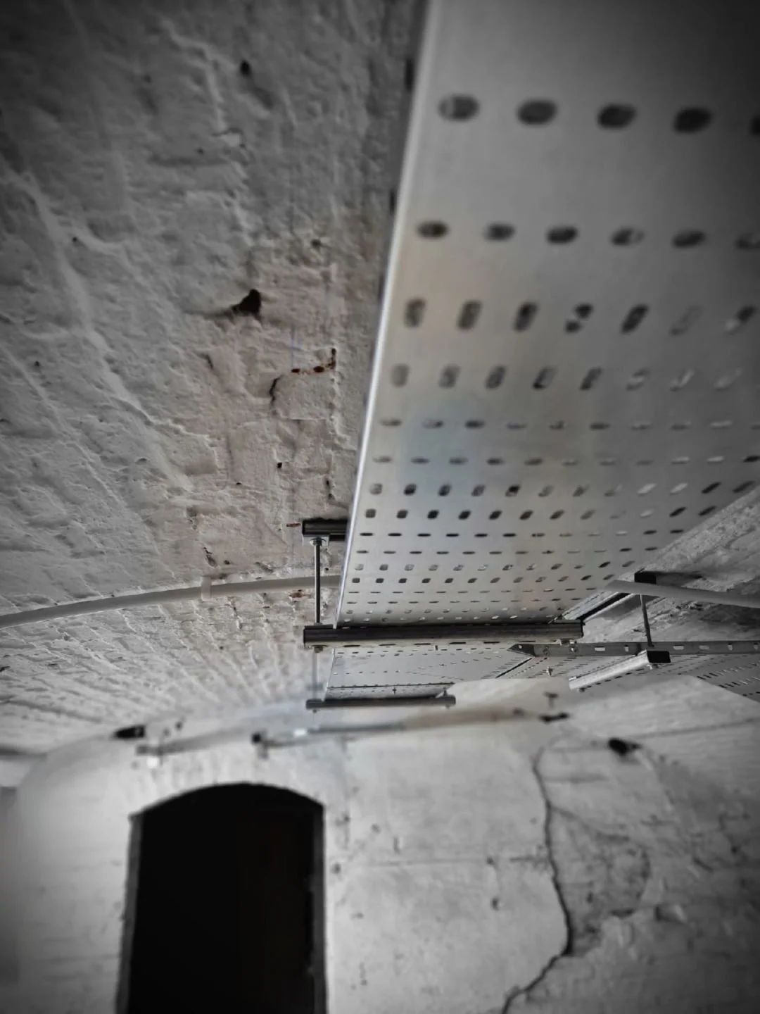 Perforated steel cable tray fixed beneath the vaulted brick ceiling of a cellar plant room, Leicester