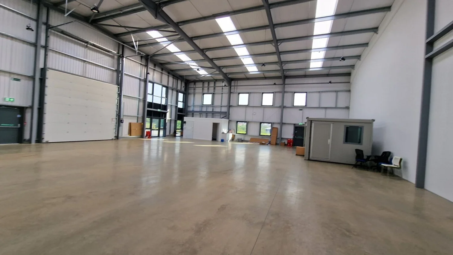 Large empty commercial unit lit by LED high bays, with a Portakabin inside, Kibworth
