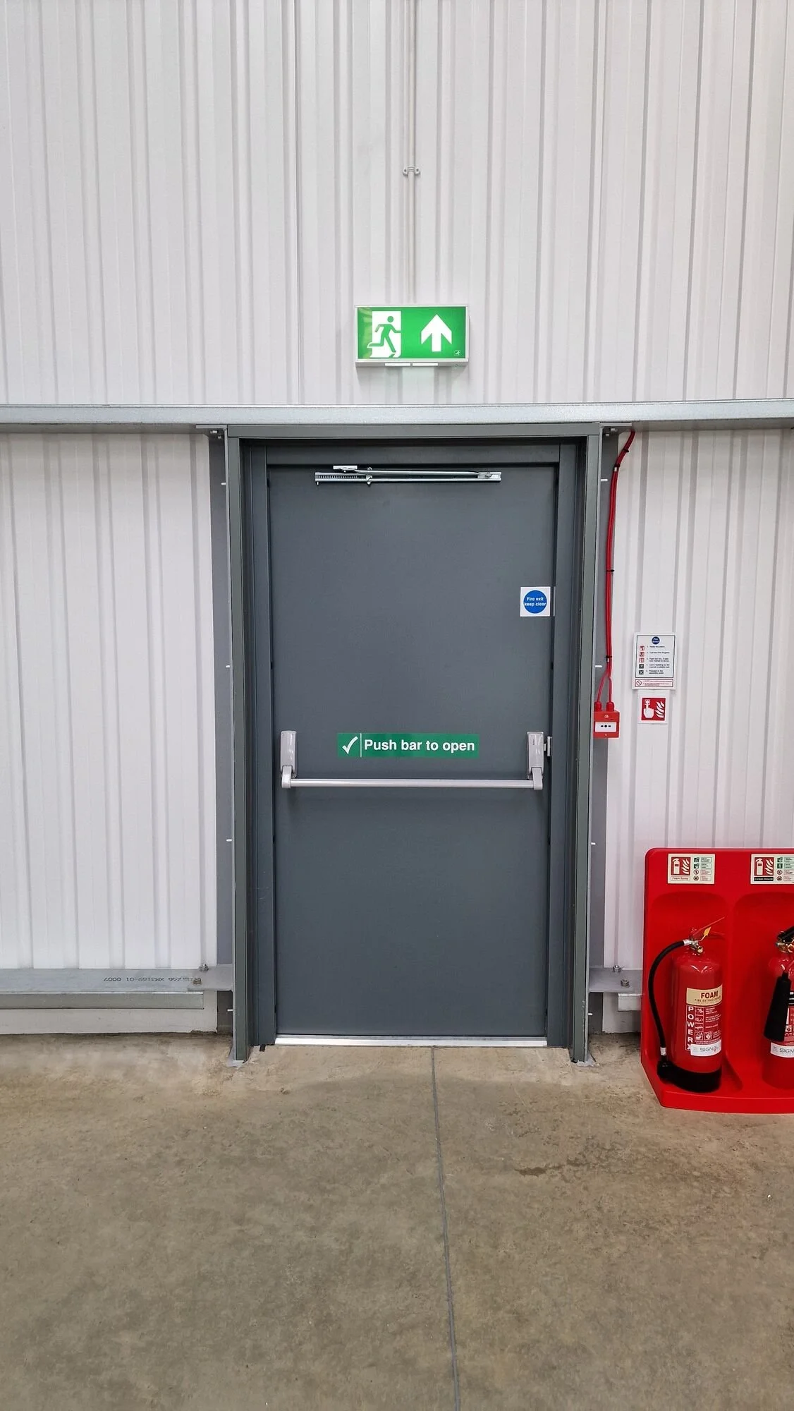 Illuminated emergency exit sign above a fire exit door in a commercial unit, Kibworth