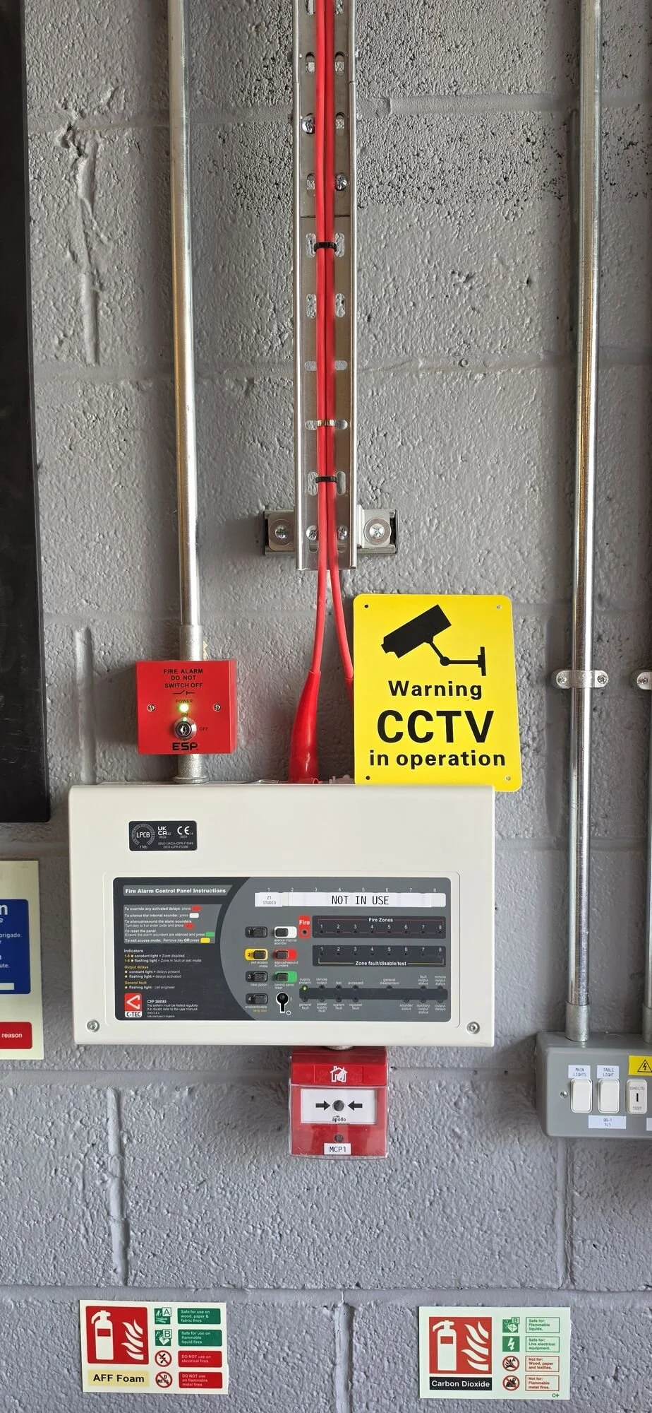 Fire alarm control panel and call point installed with red fire-resistant cable and galvanised conduit in a commercial unit, Leicester