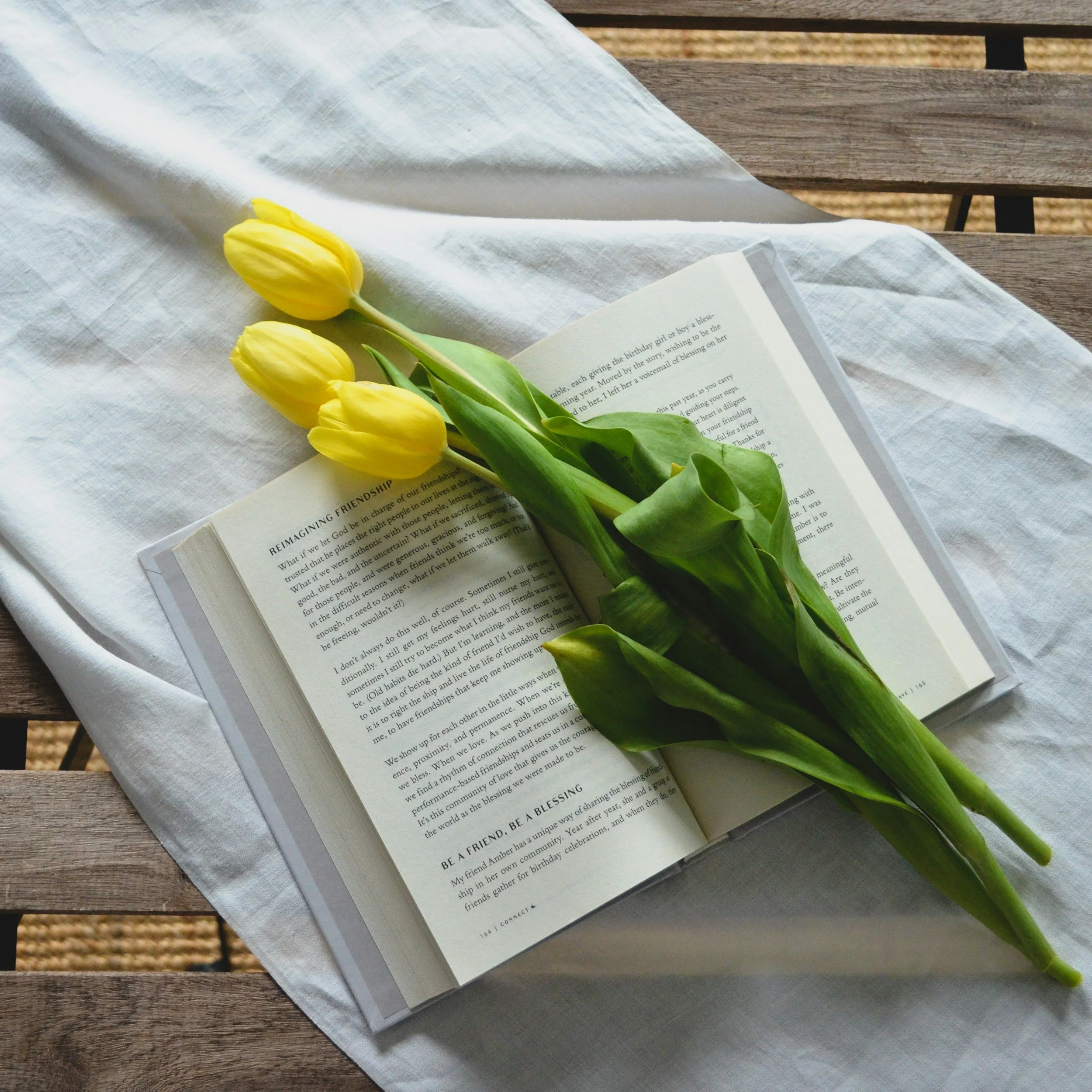 A woman with long red hair facing a lake, surrounded by tall grass and trees in the distance, with a cloudy sky.