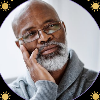 A thoughtful older African American man with glasses, a gray beard, and a gray sweater resting his head on his hand.