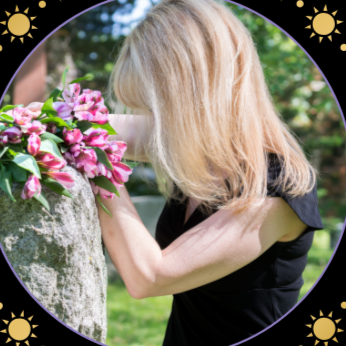 Person laying flowers on a stone memorial or tribute with sunlight and greenery in background.