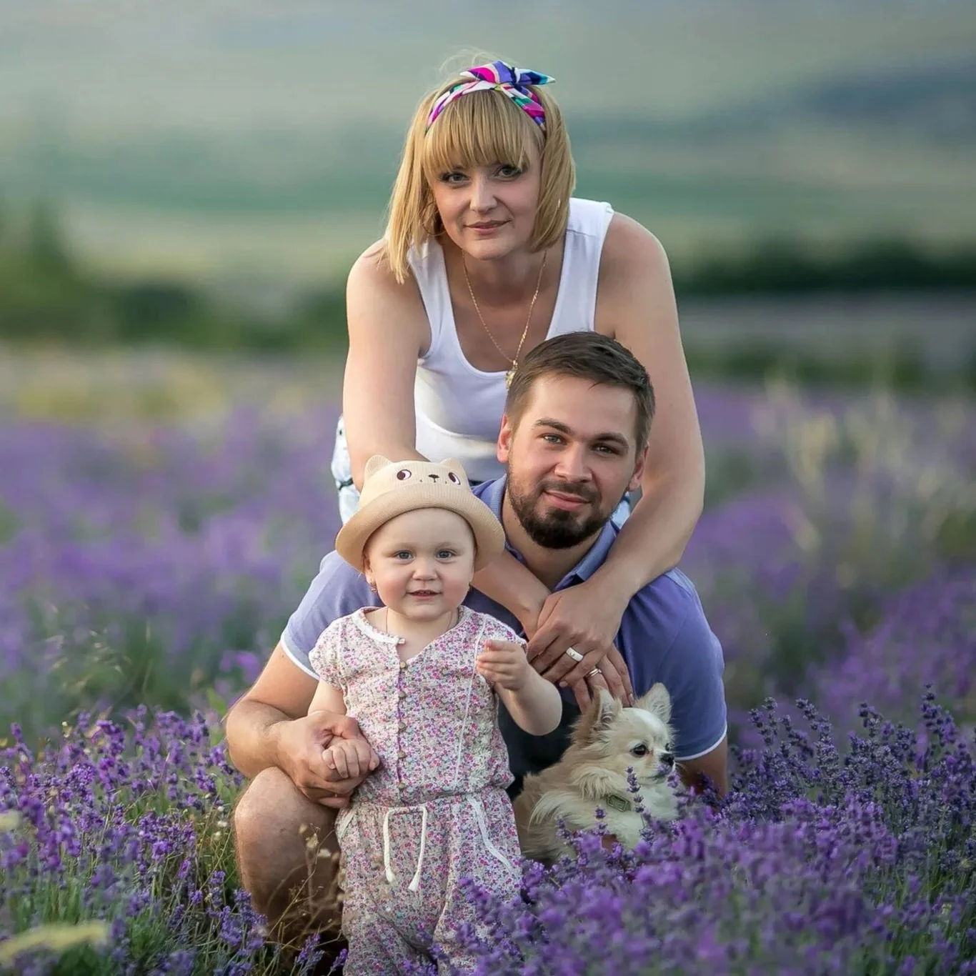 A family of four smiling and posing outdoors in a park with trees in the background.