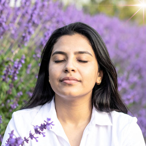 A person with blonde hair sitting on a rock, looking out at a bright sky over a mountainous landscape.
