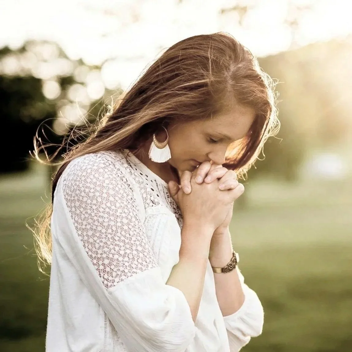 A young woman looking through window blinds with a thoughtful expression.