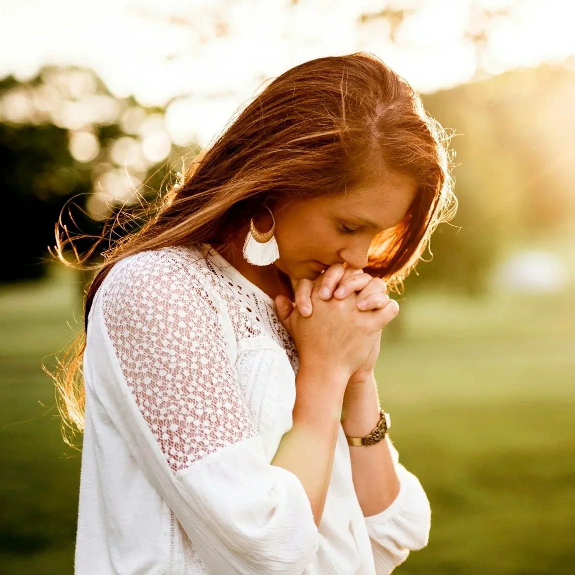 A young woman looking through window blinds with a thoughtful expression.