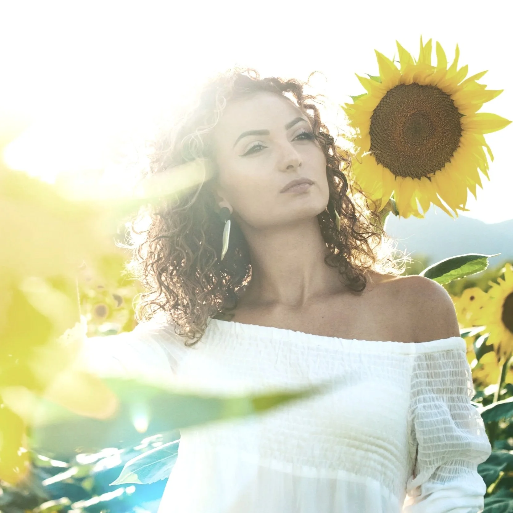 Side profile of a young man with short brown hair and a beard, wearing a dark turtleneck, sitting indoors near a window with greenery in the background.