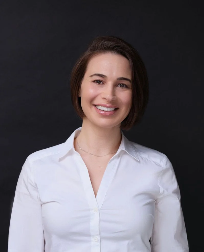 Smiling person in a white shirt against a dark background.