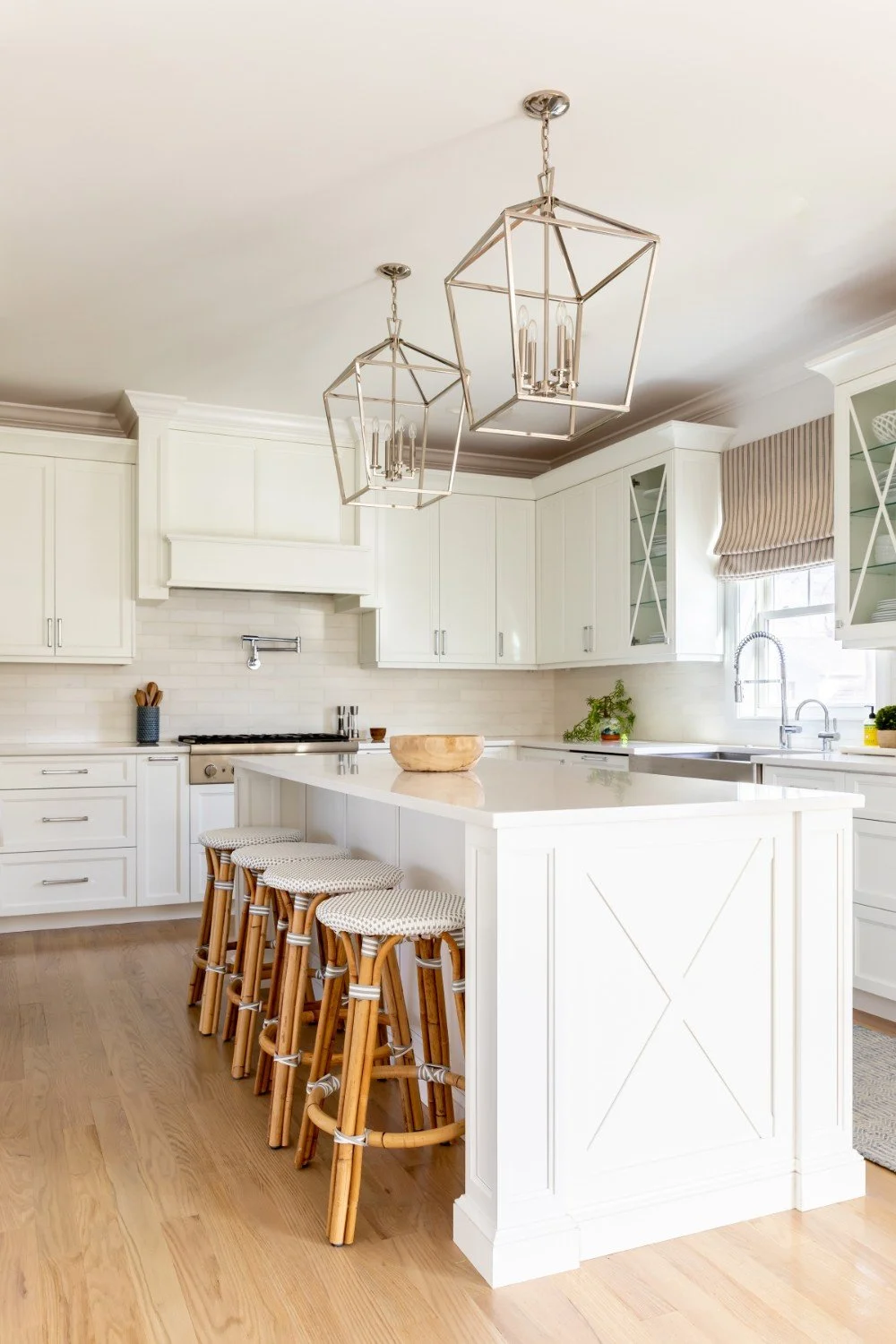 Bright, white kitchen with wooden barstools, pendant lights, and a large island counter.