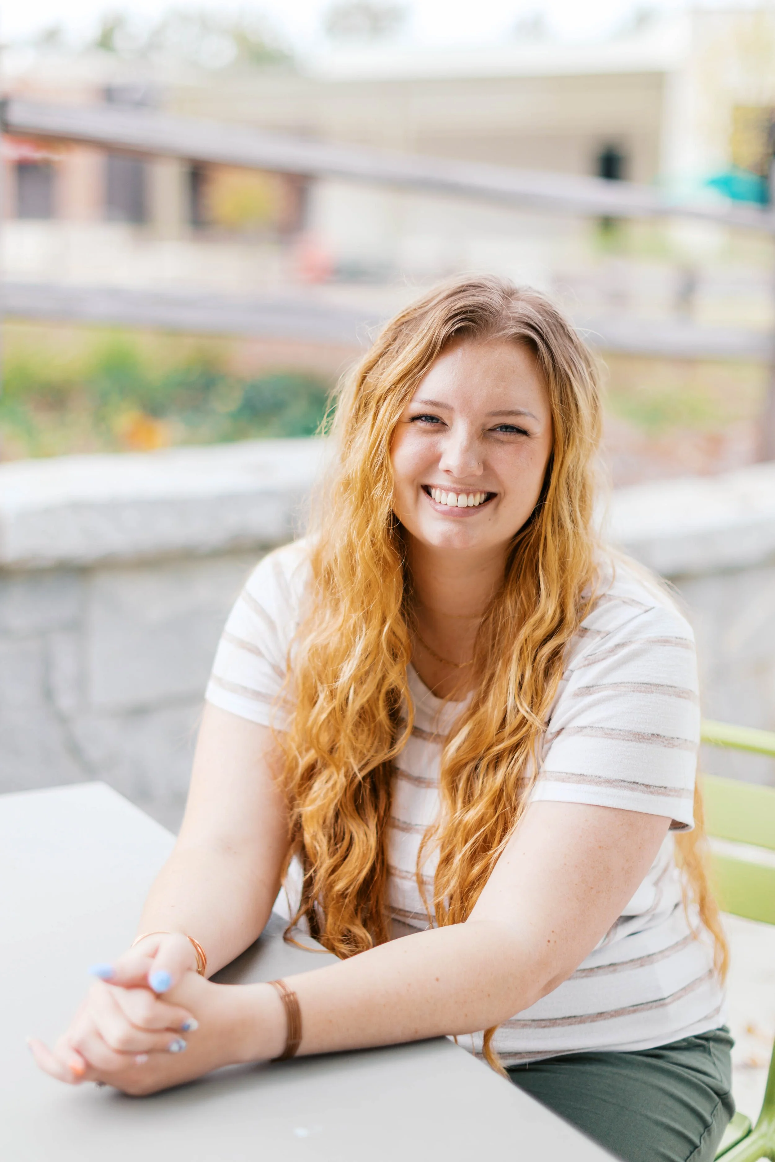 photo of shelby crews sitting at a table with her hands clasped in front of her and smiling so big her eyes squint