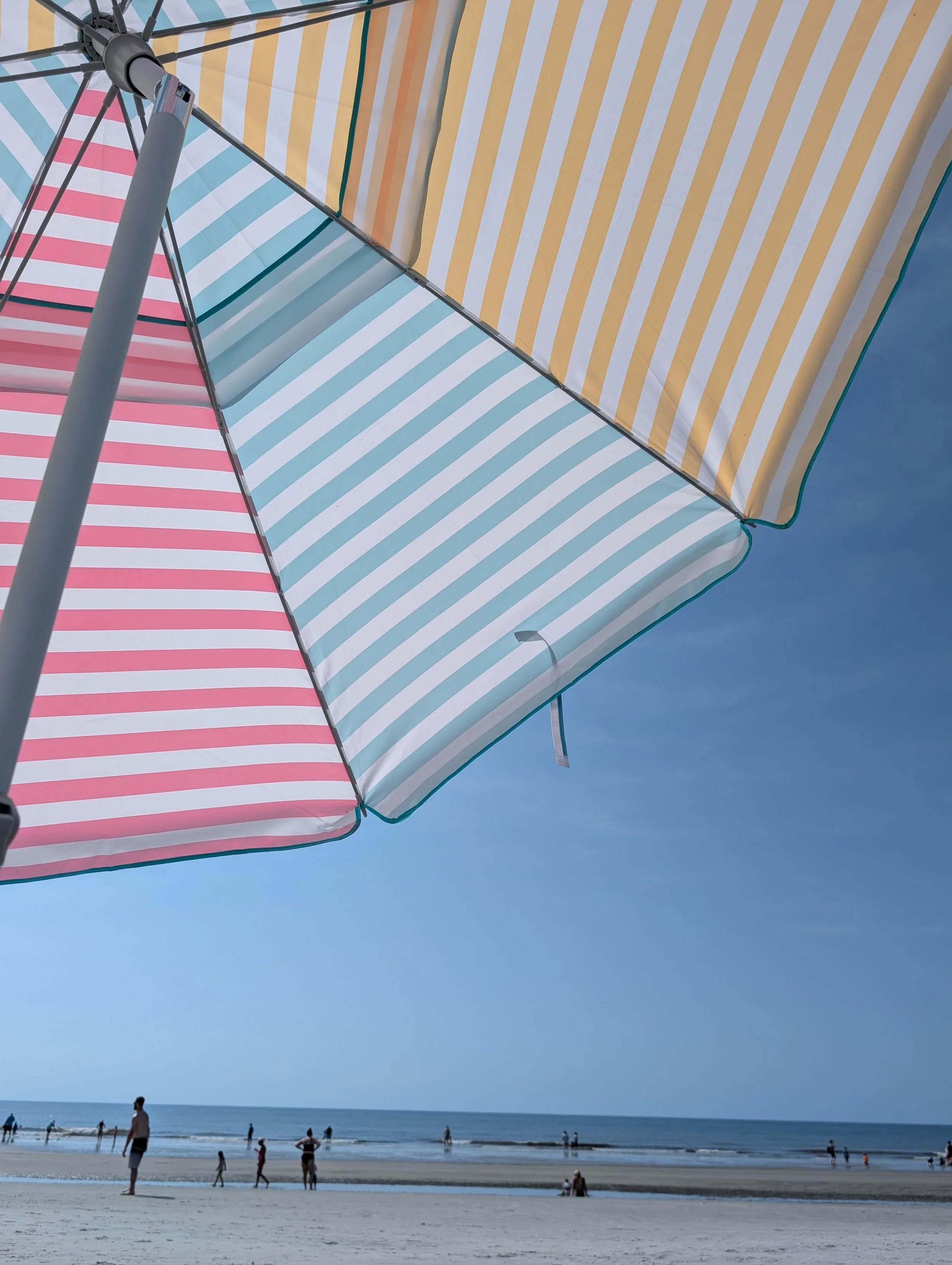 Colorful striped beach umbrellas with people on the sandy beach by the ocean under a clear blue sky.