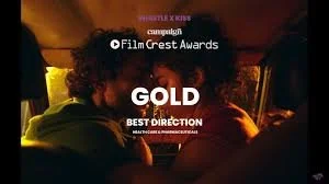 Image from the FilmCrest Awards showing a scene inside a car with two people, and text indicating a Gold award for Best Direction in Mainstream/Commercial/Entertainment.