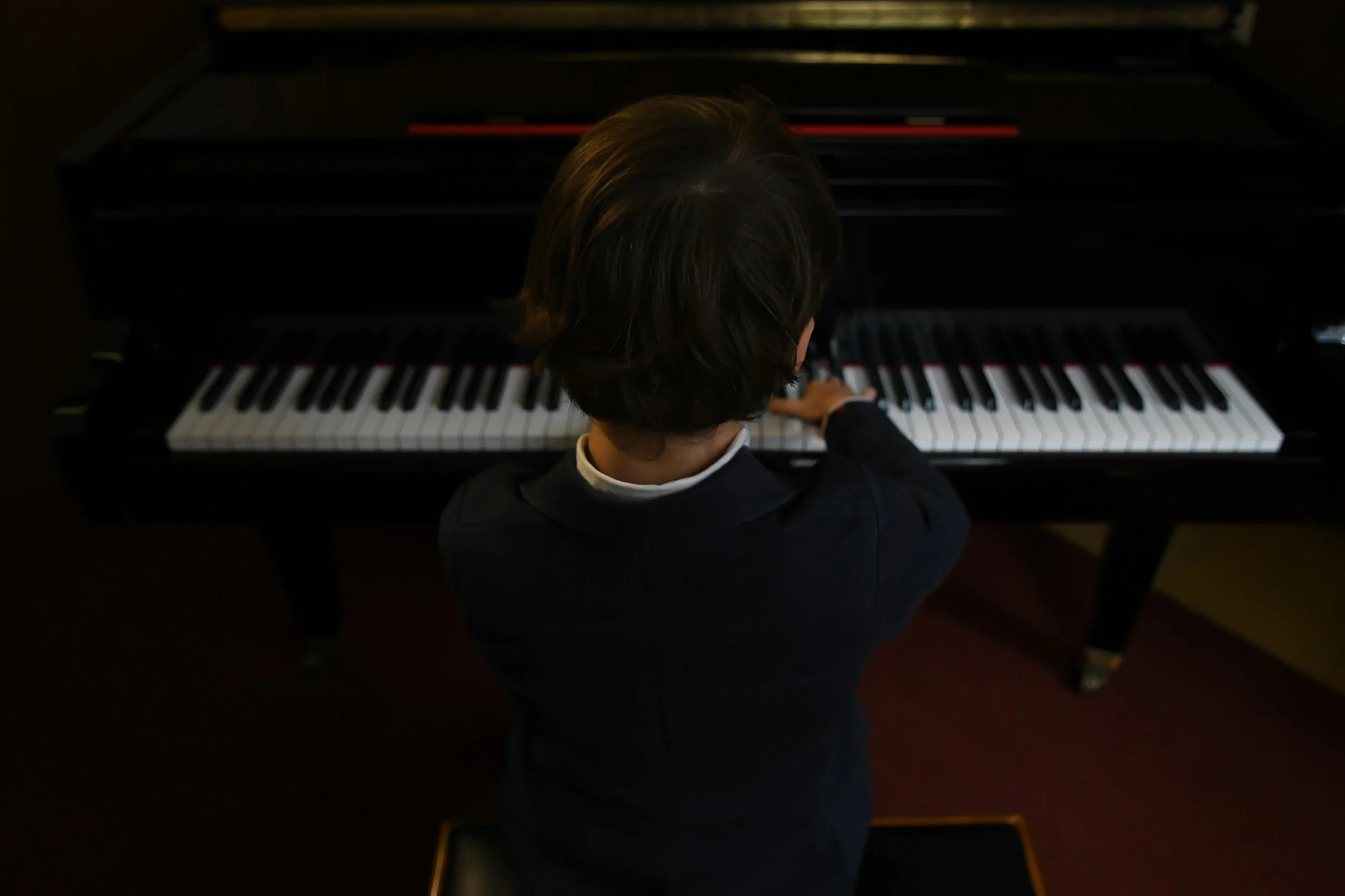 子供がオンラインレッスンでグランドピアノを弾いている後ろから写した姿