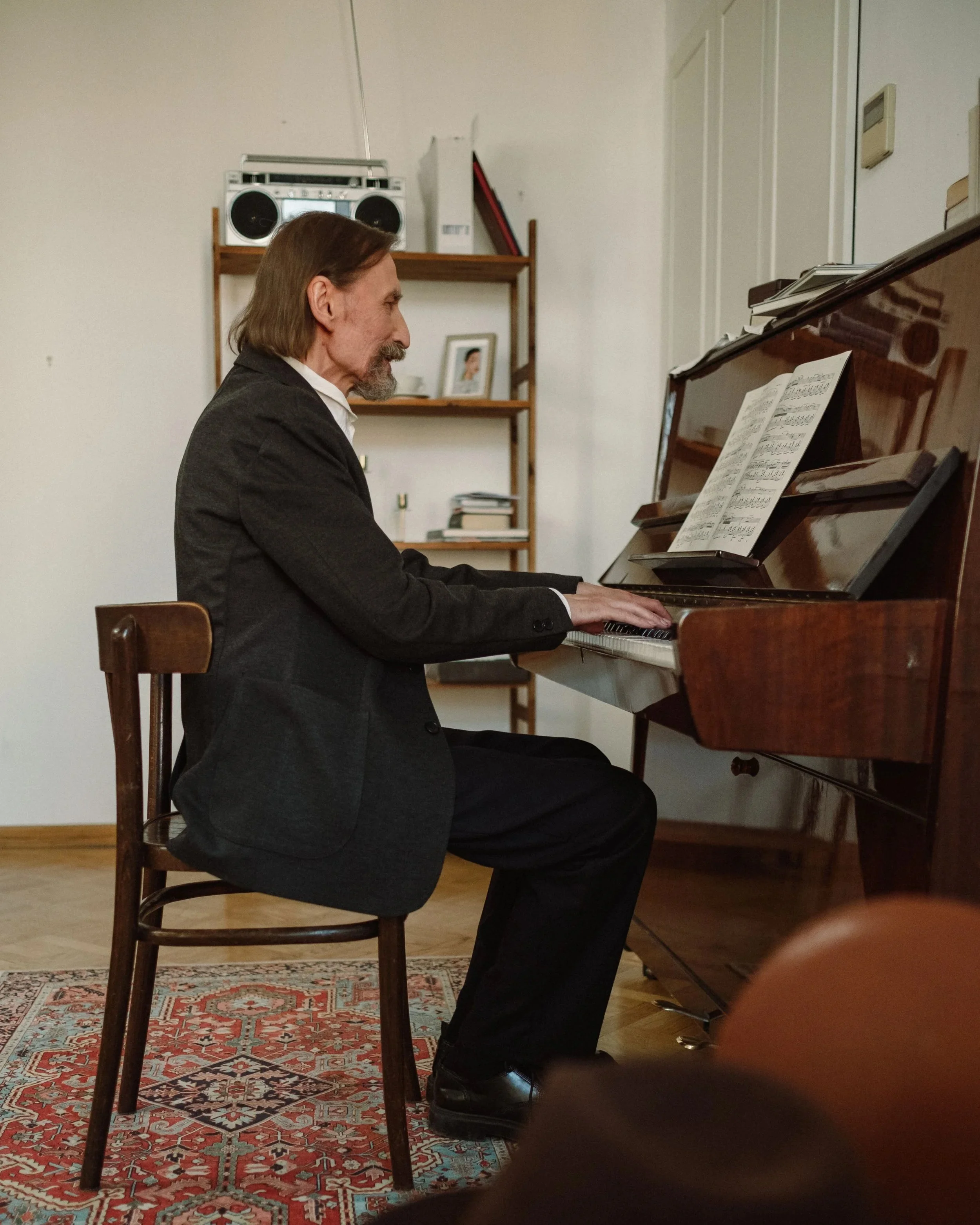 senior grandfather and granddaughter smiling at each other in front of an upright piano with sheet music