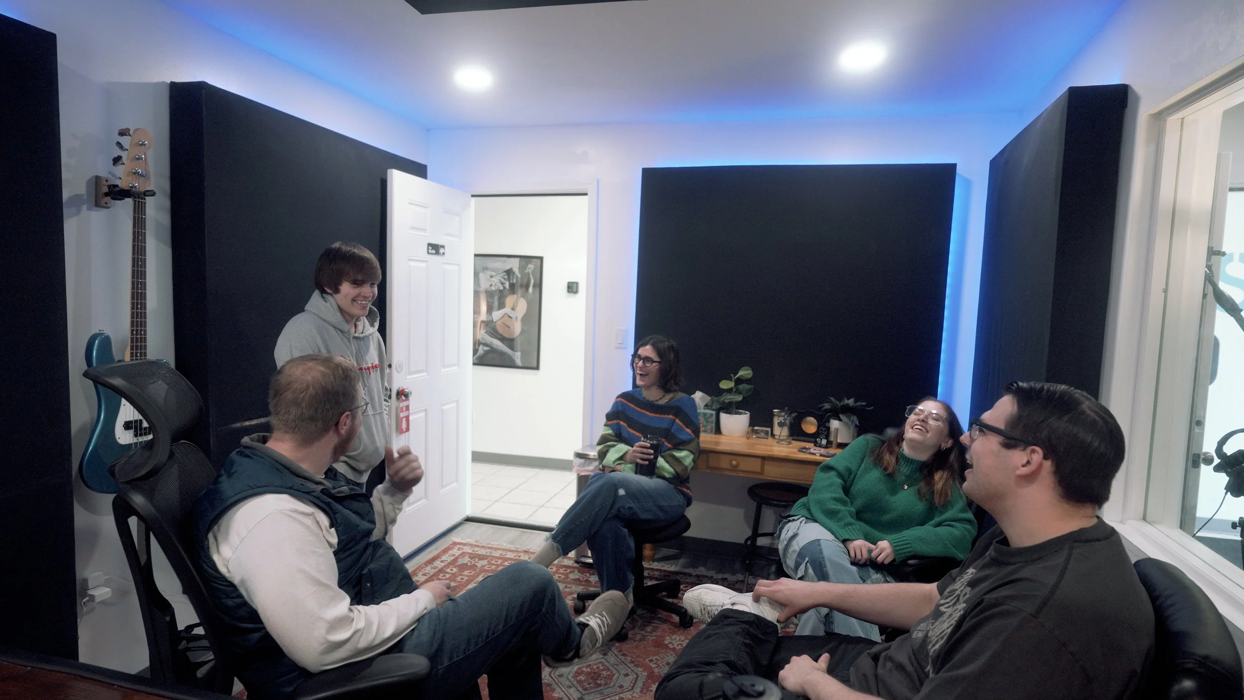 Group of friends hanging out in a music studio, chatting and laughing while seated in a circle.