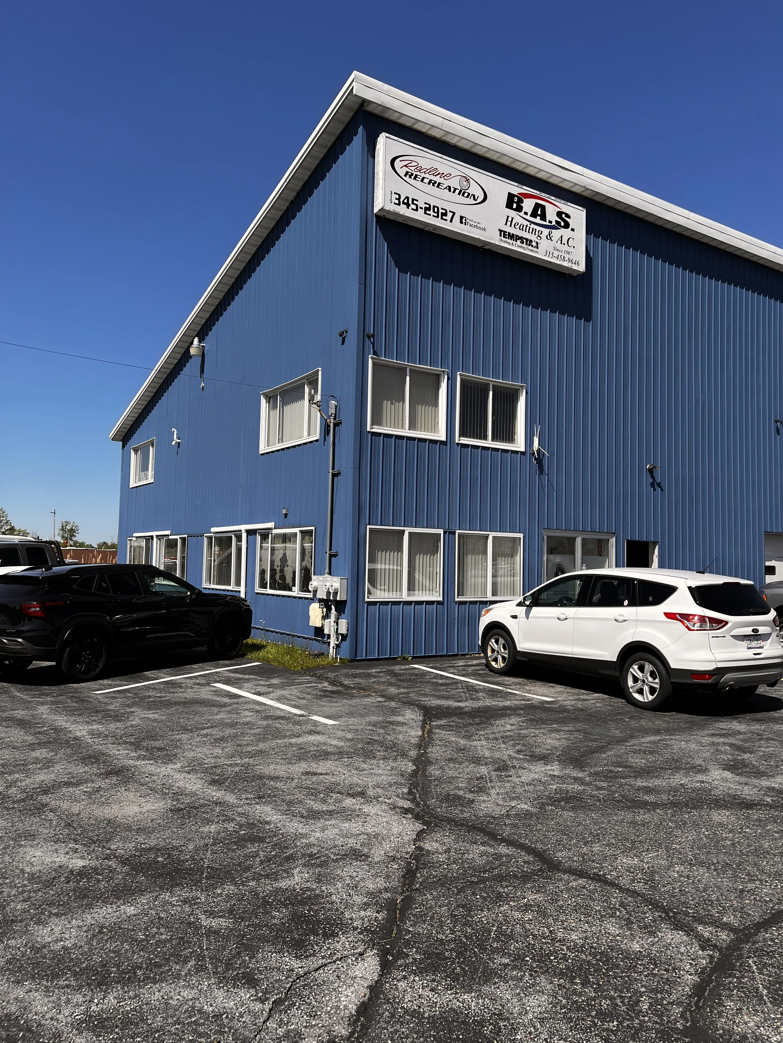 A blue commercial building with parking lot in front, three cars parked, and signs indicating heating, cooling, and recreation services.