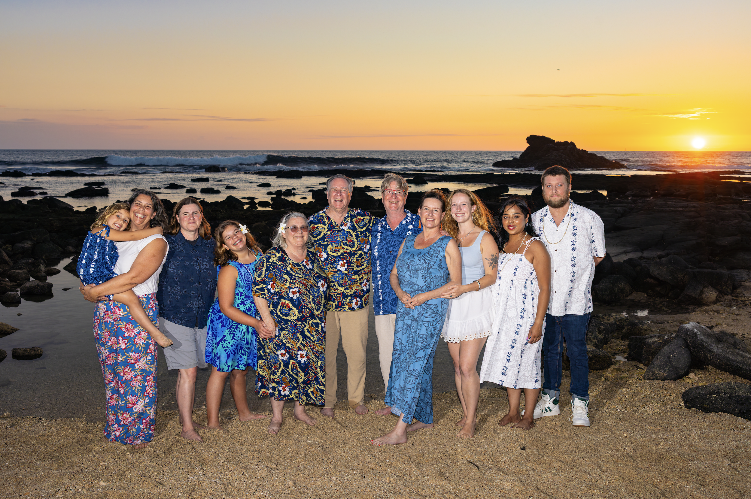 A happy group of twelve people, including children and adults, standing on a beach at sunset on the Big Island of Hawaii near Kona with their amazing family photographer Cynthia Buckles, the best photographer in Hawaii! 