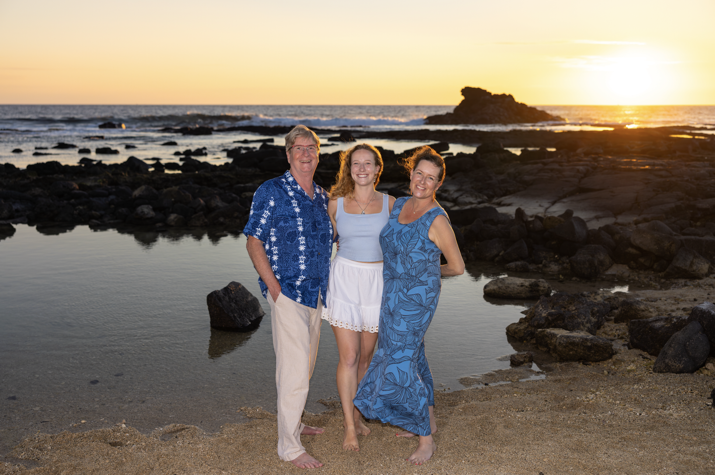 Three people standing on a beach at sunset, smiling at their photographer Cynthia Buckles with CynthiArtistry. Cynthia Buckles is rated best photographer on the Big Island of Hawaii near Waimea, Waikoloa and Kona.
