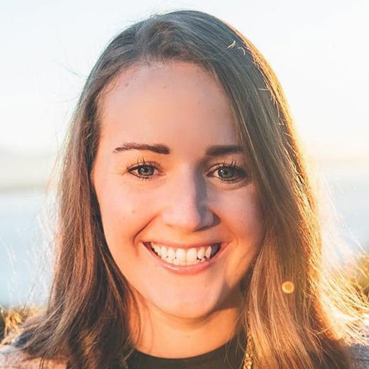 A smiling young woman outdoors during sunset with long brown hair.