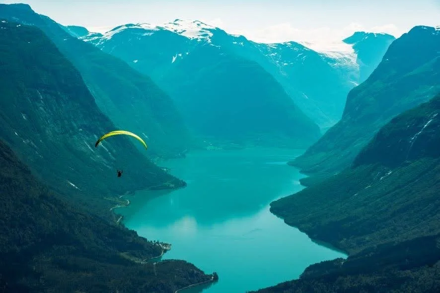 parasailer in flight in mountains of Norway, floating down towards a fjord