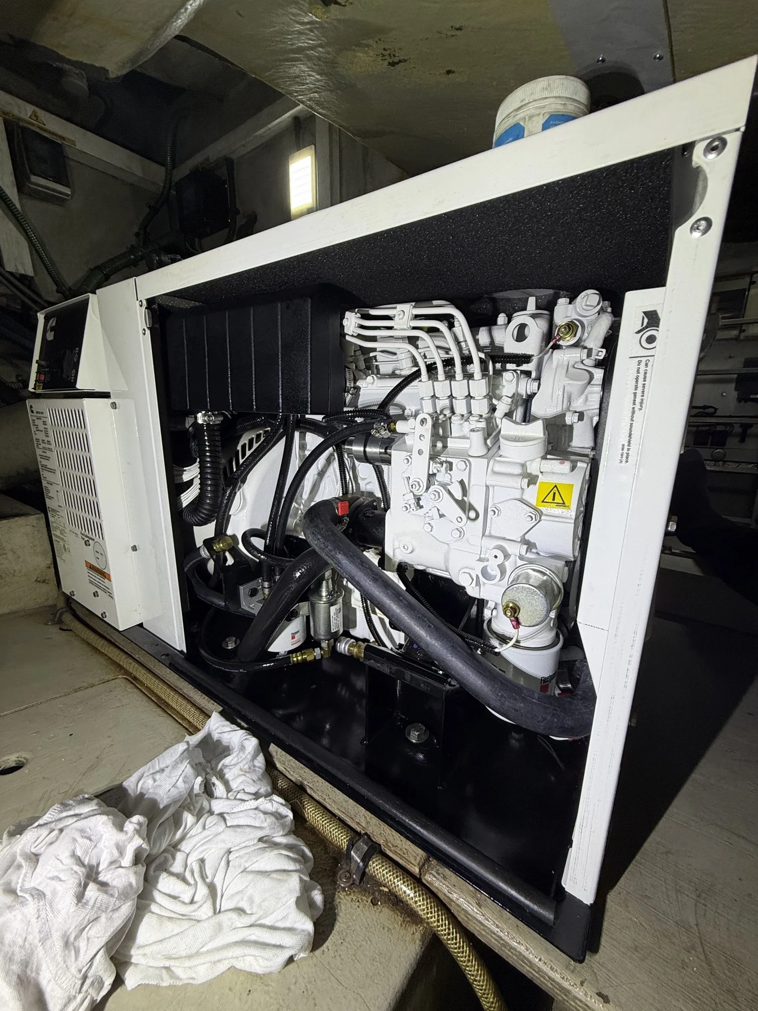 Close-up of a white industrial machine with black panels and various metal pipes and connectors inside a workshop. The machine is positioned on a concrete floor with cloths beneath it.