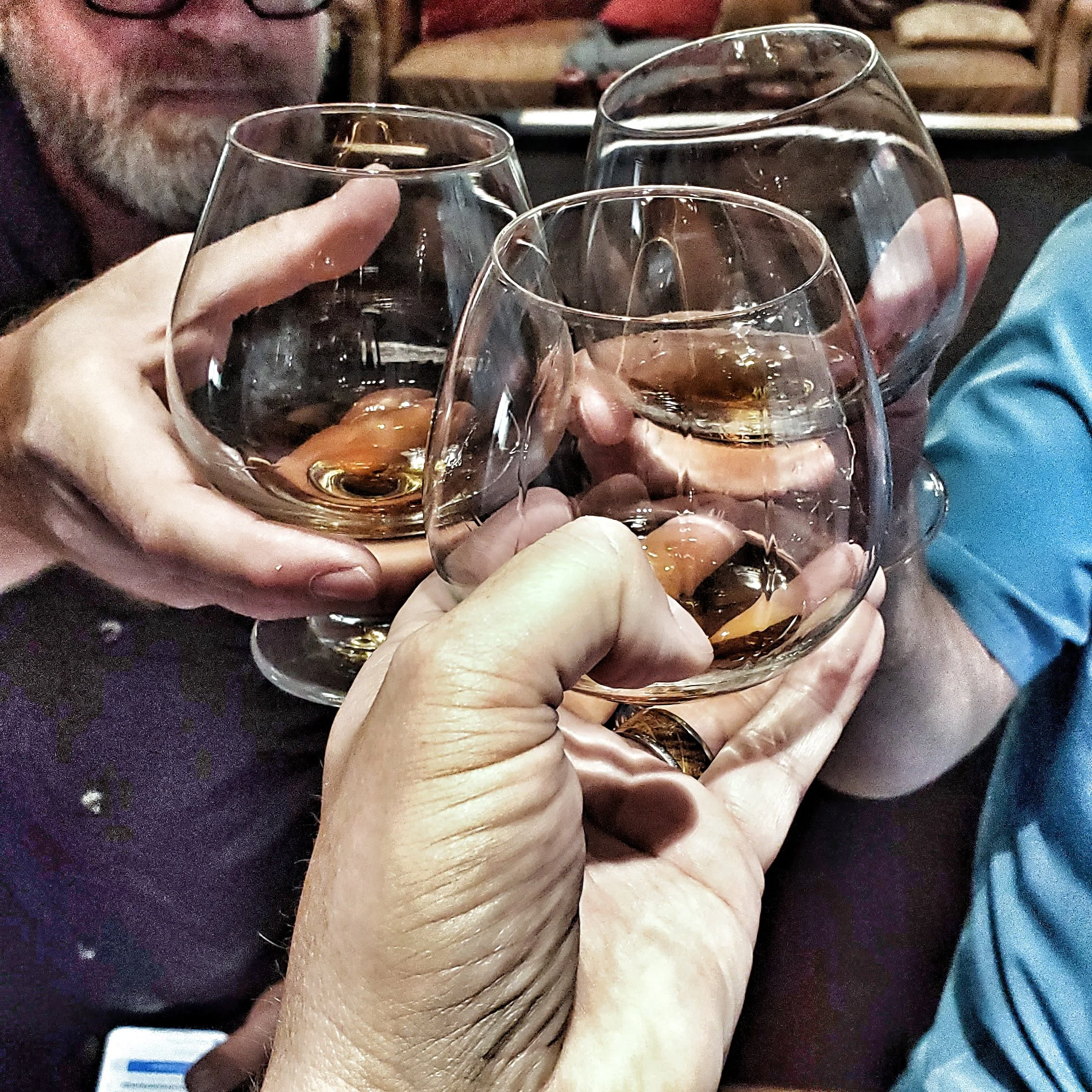 Three brandy glasses being toasted together by friends.