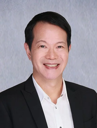 Headshot of a smiling man in a suit and white shirt against a light background.