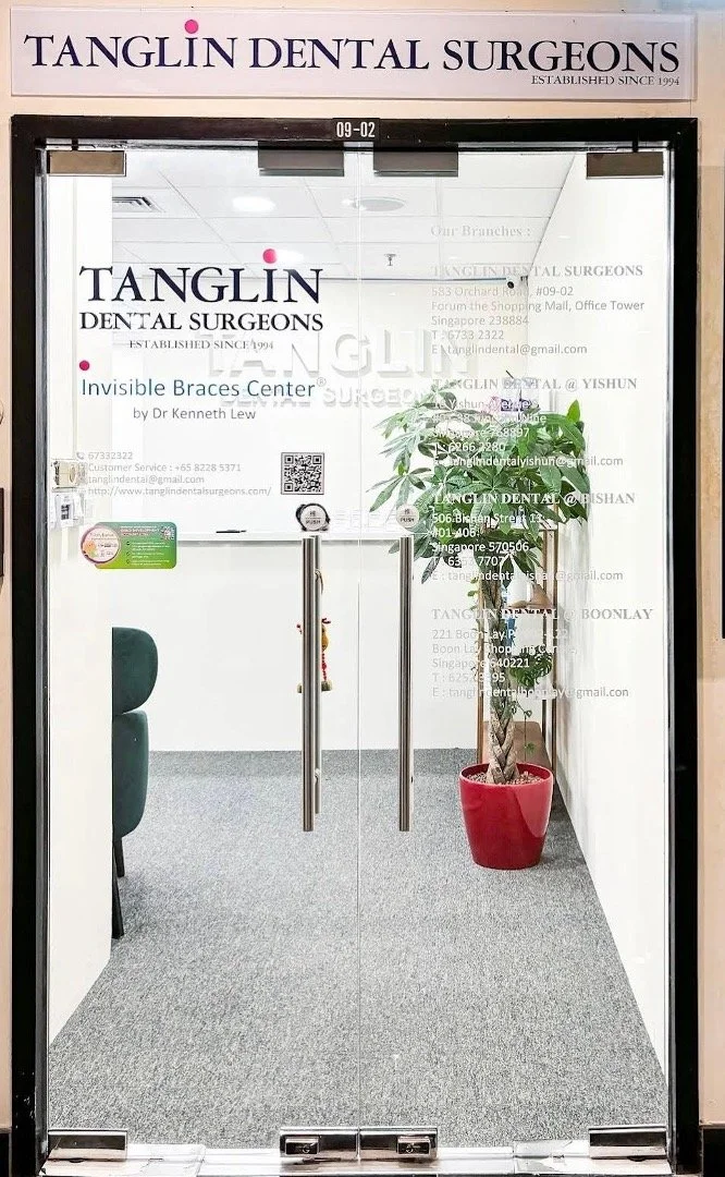 Glass door entrance to Tanglin Dental Surgeons with signage, a potted plant on the right, and an office waiting area inside.