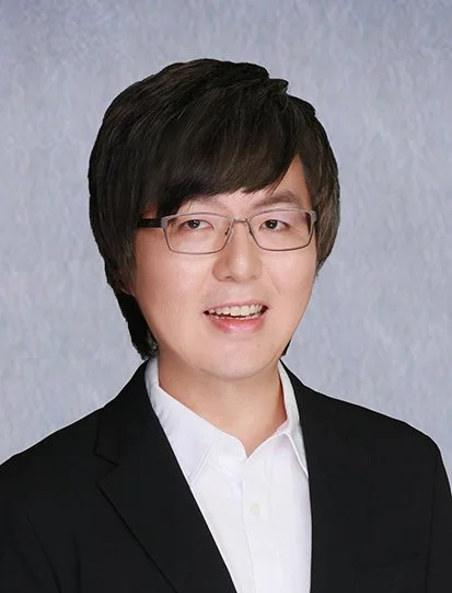 Professional portrait of a young man in a business suit, wearing glasses and a watch, smiling with arms crossed.