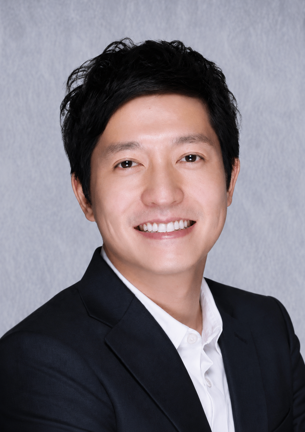一位黑发青年身穿浅蓝色纽扣衬衫,双臂交叉,面带微笑,背景为素雅的浅色。
