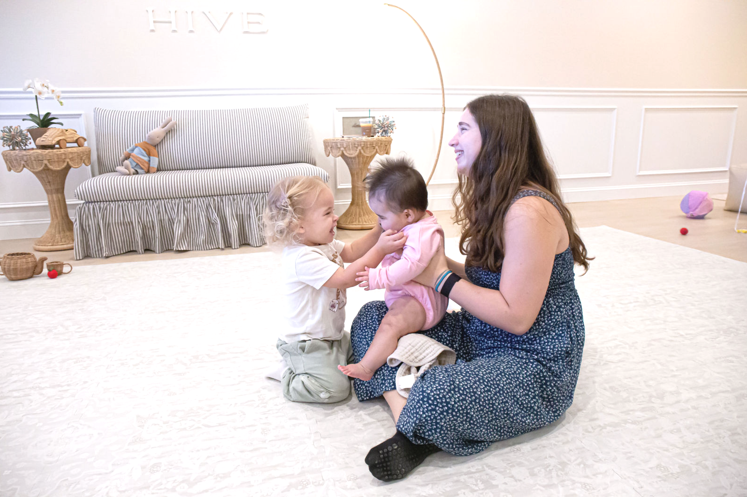 two moms sitting down laughing with their children crawling all over them