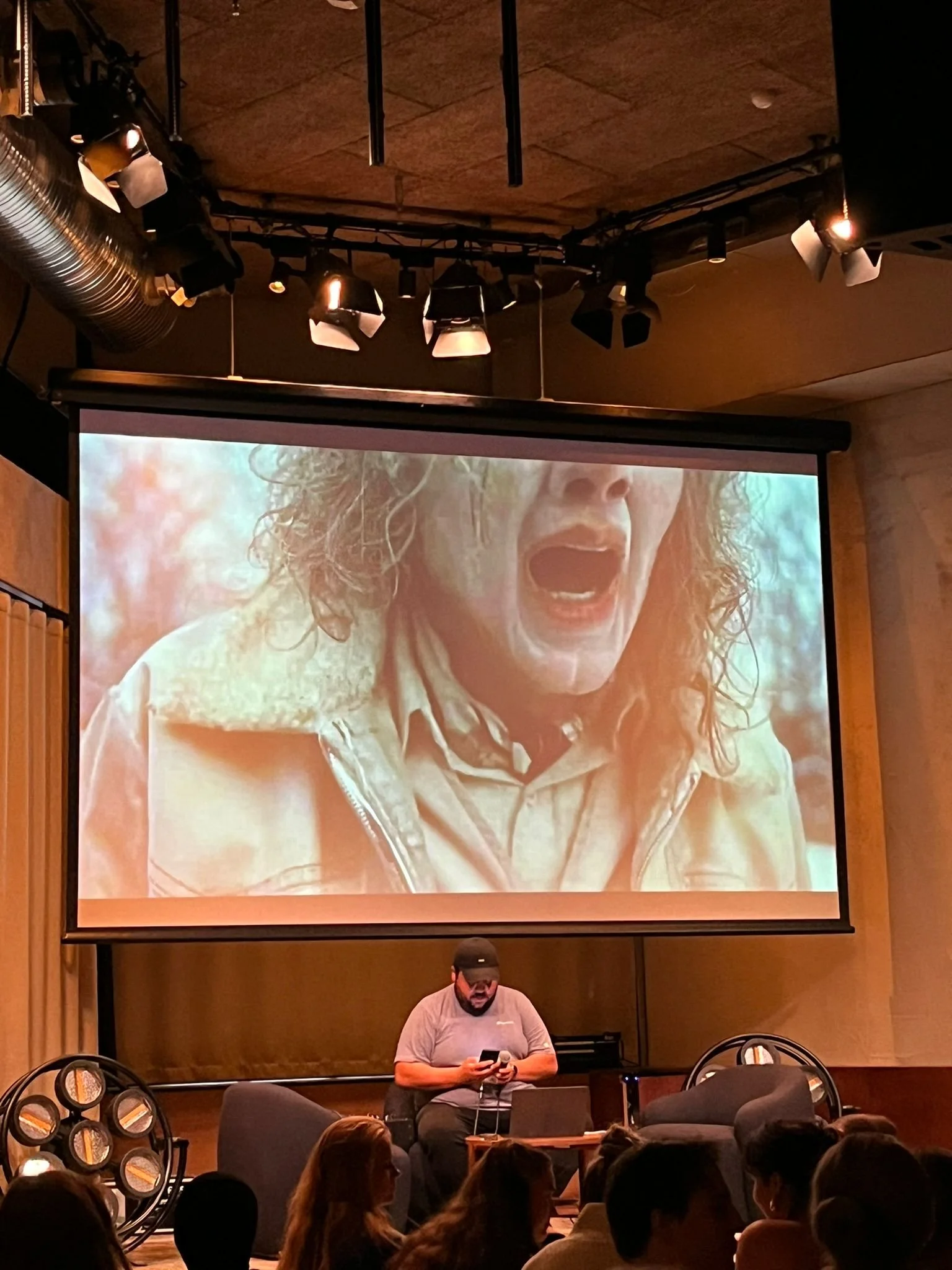 Javad sitter foran en skjerm på en scene og styrer quizen med mobilen sin.