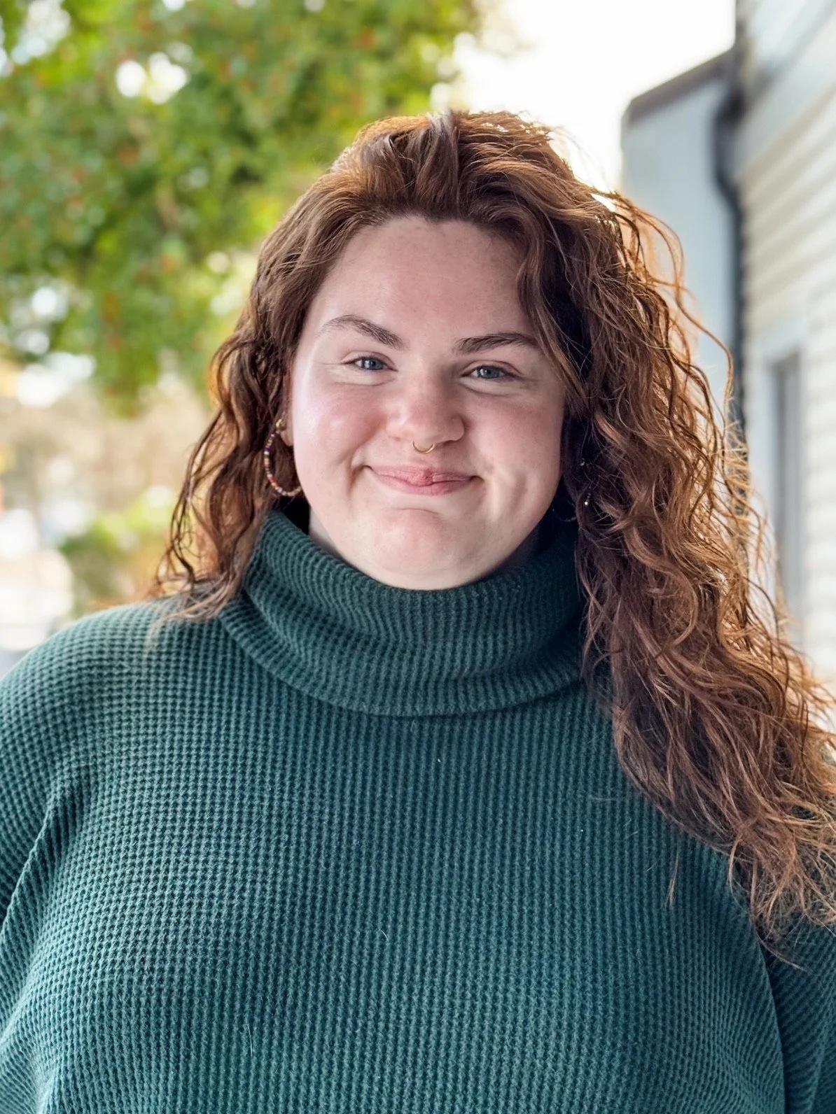 Caitlyn Barnes stands outside smiling in a dark green turtleneck sweater
