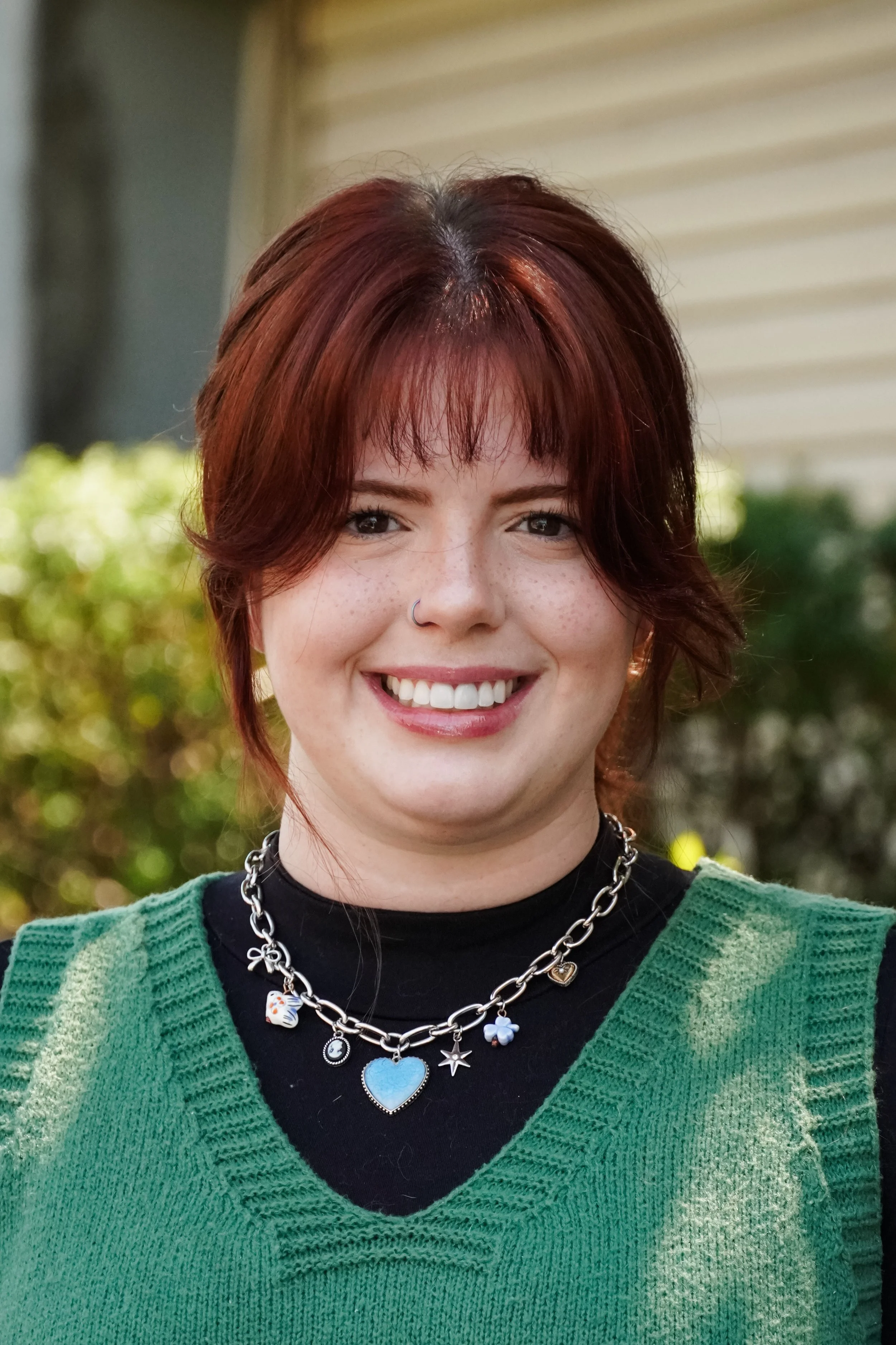 A woman stands smiling with red hair, a green shirt